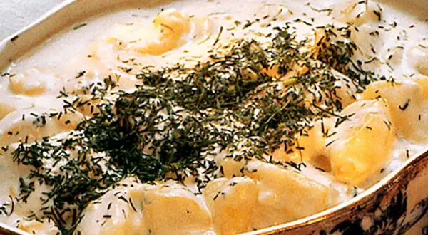En krämig stuvad potatis med dill, serverad i ett vackert fat. En klassisk svensk rätt som värmer själen.