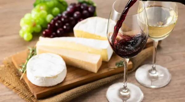 Un bicchiere di vino rosso viene versato, accanto a formaggi assortiti e grappoli d'uva. L'abbinamento perfetto di vino per formaggi.