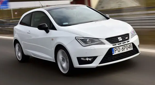 Biały Seat Ibiza 1.4 benzyna pędzi po drodze, z czarnym dachem i felgami.