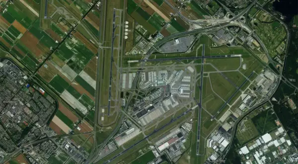 Widok z lotu ptaka na lotnisko Schiphol w Amsterdamie, otoczone polami i drogami.