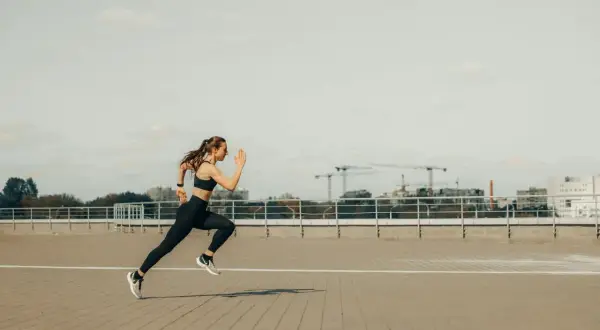 Kobieta w sportowym stroju biegnie, pokonując dystans 5 km. W tle widać miejską panoramę z dźwigami budowlanymi.