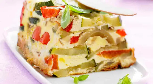Tranche de terrine de légumes colorée, avec courgettes, poivrons rouges et une touche de basilic frais.