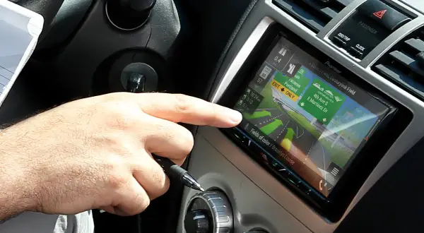 Dłoń kierowcy dotyka ekranu nawigacji z mapą, która wygląda jak z systemu radio android auto.