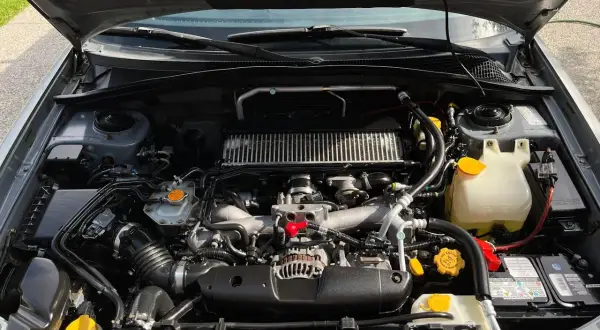 Silnik Subaru z widocznym zbiorniczkiem płynu chłodniczego. Sprawdzanie, ile mieści się płynu w chłodnicy, jest kluczowe dla jej prawidłowego działania.