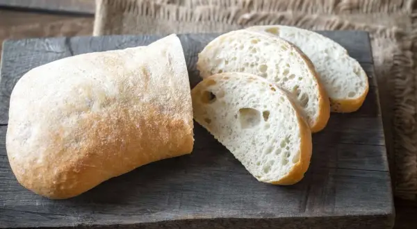 Ein rustikales ciabatta mit sauerteig, aufgeschnitten auf einem Holzbrett.
