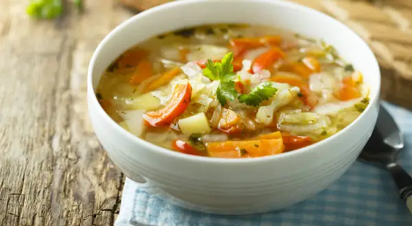 Aromaticzna jarzynowa zupa z kawałkami marchewki i ziemniaków, udekorowana natką pietruszki, podana w białej misce na drewnianym stole.