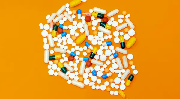 Rozsypane tabletki i kapsułki, w tym leki opioidowe, na pomarańczowym tle.