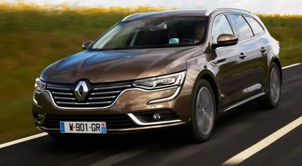 Brązowe renault talisman kombi pędzi po drodze, mijając pola.