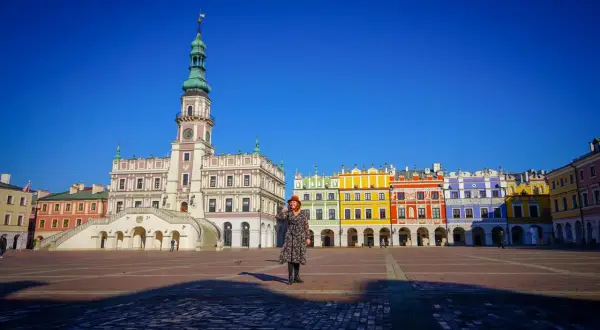 Kobieta w czerwonym kapeluszu na Rynku Wielkim w Zamościu, podziwiająca renesansową architekturę. Stare miasto w Zamościu zachwyca kolorowymi kamienicami.