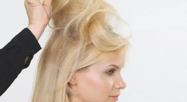 Blonde Frau mit voluminösen Brigitte Bardot Haaren, die von einer Hand mit einem Kamm gestylt werden.