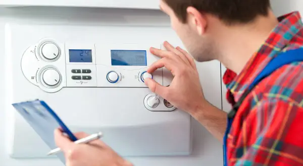 Tecnico regola la temperatura acqua sanitaria su una caldaia, con appunti in mano.