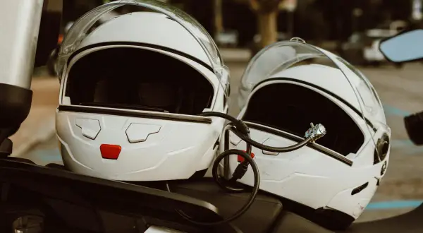 Dwa białe kaski motocyklowe połączone linką zabezpieczającą. Mocowanie kasku do motocykla zapewnia bezpieczeństwo podczas postoju.
