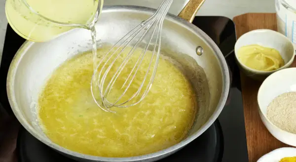 Flüssigkeit wird in eine Pfanne mit einem Schneebesen gegossen, um eine cremige vegane Hollandaise zuzubereiten.