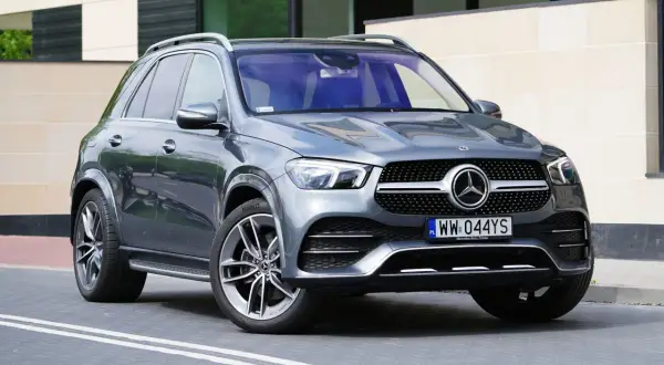 Szary Mercedes GLE 300 d stoi przed nowoczesnym budynkiem. Elegancki SUV z charakterystycznym grillem i felgami.