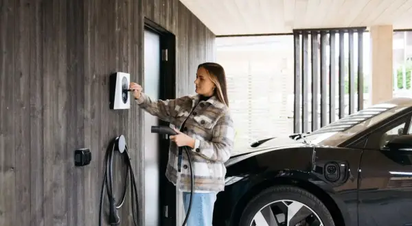 Kvinna laddar elbil vid laddbox. Frågan "hur lång tid tar det att ladda en elbil 22kw" är relevant här.