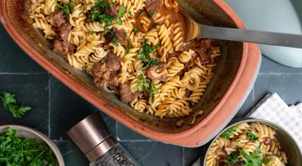 Herzhaftes Gulasch mit Nudeln, garniert mit frischer Petersilie, serviert in einem rustikalen Auflauf.