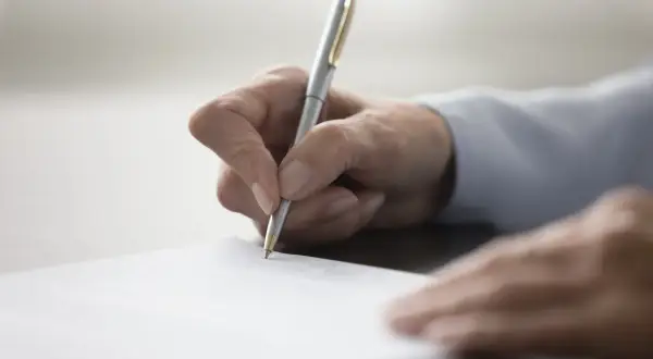 Dłoń pisze długopisem na dokumencie, finalizując umowę przyrzeczoną.