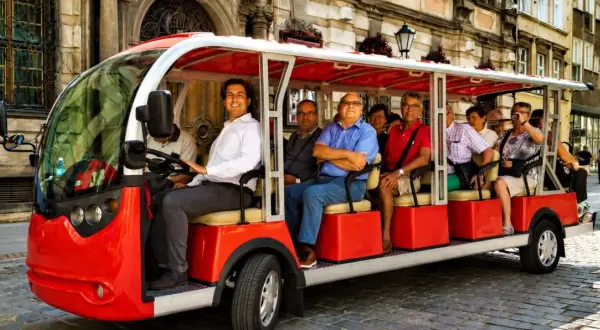 Eine Gruppe von Touristen genießt eine entspannte Stadtrundfahrt in Breslau mit einem roten Elektro-Tourbus.