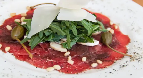 Delicato carpaccio di manzo con rucola, scaglie di parmigiano, pinoli, capperi e funghi champignon.