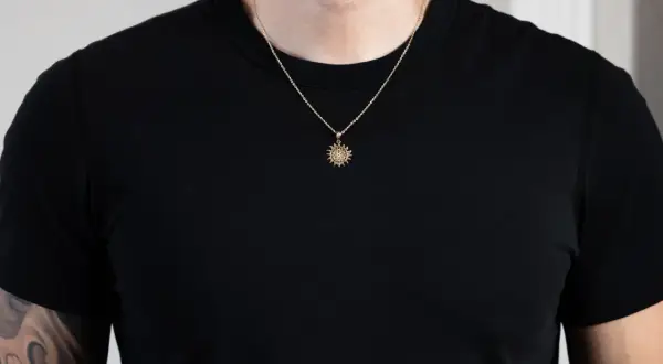 Un hombre luce un colgante sol oro con detalles intrincados sobre una camiseta negra.