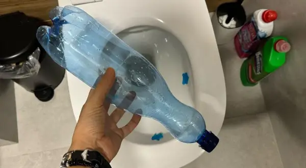 Ręka trzyma plastikową butelkę nad toaletą, pokazując, jak odetkać toaletę bez przepychaczki.