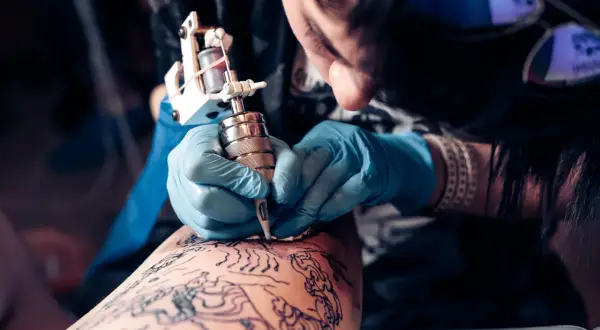 Artista tatuando en la convención de tatuajes Valencia. Manos enguantadas trabajan con precisión sobre un diseño en la piel.