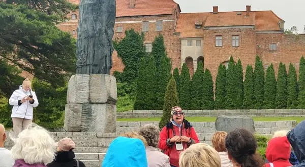 Wycieczka po Fromborku: przewodnik opowiada o Koperniku przy pomniku, w tle katedra. Atrakcje Fromborka odkrywane przez turystów.