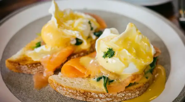 Zwei pochierte Eier auf Toast mit Lachs und Sauce Hollandaise. Ein köstliches pochierte Eier Rezept für ein perfektes Frühstück.