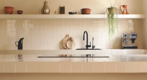 Encantadora cocina con azulejos claros, grifo negro y cafetera. Las últimas tendencias en azulejos para cocinas se reflejan en este diseño minimalista y funcional.