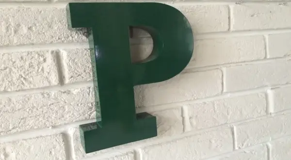 Une lettre murale verte en forme de P est fixée sur un mur de briques blanches.