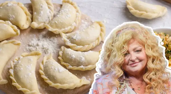 Magda Gessler prezentuje przepis na ciasto na pierogi. Na zdjęciu surowe pierogi na desce i uśmiechnięta restauratorka.