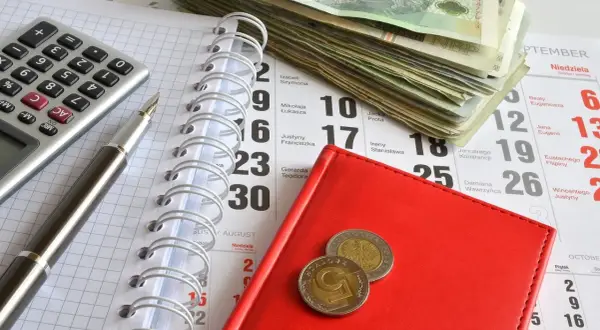 Kalkulator, długopis, stos banknotów i monety na kalendarzu. Przygotowanie do zapłaty opłaty od pozwu w postępowaniu upominawczym.