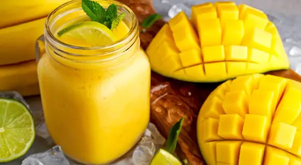 Orzeźwiający koktajl z mango, udekorowany miętą i limonką, obok pokrojonych owoców i bananów.
