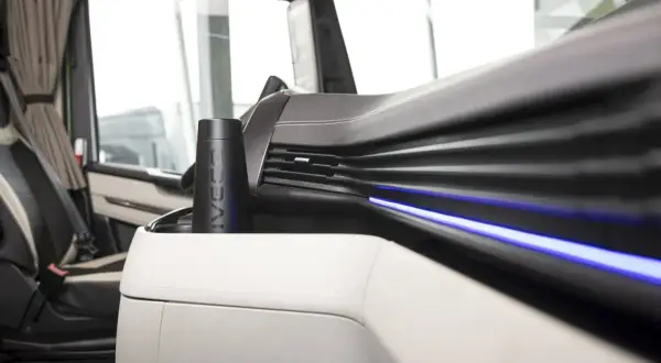 Un porte-gobelet noir avec le logo IVECO, un des indispensables du routier, est placé sur la console centrale d'un camion.