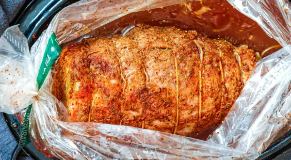 Soczysta szynka pieczona w rękawie, przyprawiona i związana sznurkiem, gotowa do pieczenia w aromatycznym sosie.