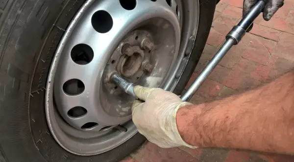 Main tenant utilise une clé pour changer un pneu.