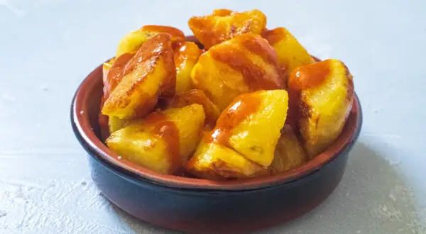 Knusprige Kartoffelstücke, überzogen mit einer würzigen Sauce, serviert als köstliche Patatas Bravas in einer rustikalen Schale.