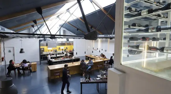 Interior de un restaurante con cocina abierta y estanterías de vino. Un lugar ideal para disfrutar de una experiencia Bib Gourmand en Zaragoza.