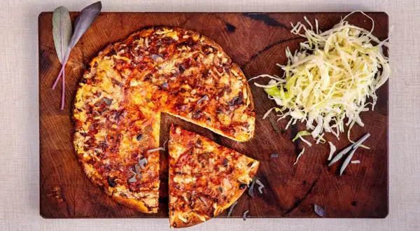 En hel och en skivad pizza på en träskärbräda, med en hög strimlad kål. En klassisk kombination som ger en hint om pizzasallad ursprung.