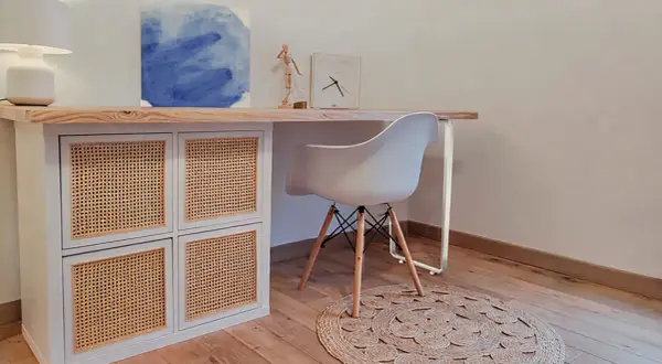Bureau en pin relooké avec des portes en rotin. Une chaise blanche et un tapis rond complètent ce coin bureau moderne.