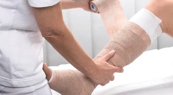 Fachkraft übt Kompressionsverband Techniken an einem Bein aus. Der Verband stützt und stabilisiert.