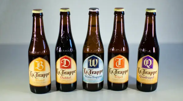 Cinque bottiglie di birra La Trappe, tra cui Blond, Dubbel, Witte Trappist, Tripel e Quadrupel, disposte in fila.