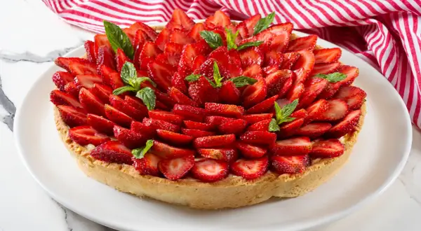 Deliziosa crostata alla crema, ricoperta da fragole fresche affettate e guarnita con foglie di menta.
