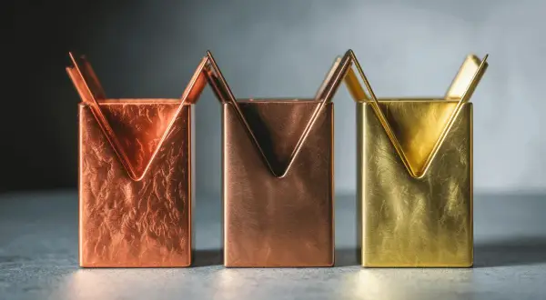 Trois porte-stylos aux formes géométriques, en laiton et cuivre, aux textures variées.