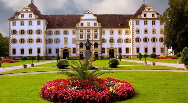 Prachtvolles Schloss Salem mit symmetrischer Fassade, gelben Akzenten und einem gepflegten Garten voller Blumen und Bäume.