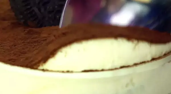 Une cuillère plonge dans un délicieux tiramisu Oreo, saupoudré de cacao. Un dessert gourmand à savourer !