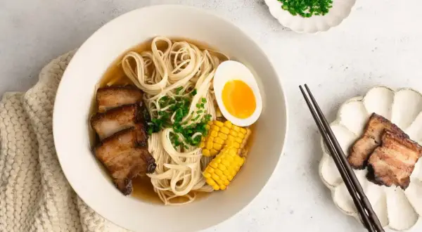 A miseczce shoyu ramen z makaronem, plastrami boczku, jajkiem na pół, kukurydzą i szczypiorkiem.