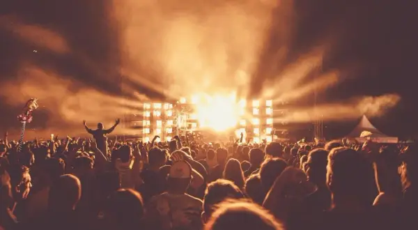 Tłum ludzi na Sunrise Festival Poland, z rękami w górze, w blasku świateł scenicznych i dymu.