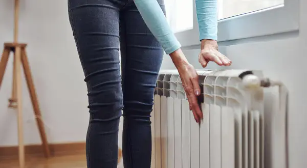 Mani che toccano un termosifone freddo, preoccupazione perché i termosifoni non si scaldano e la casa è gelida.