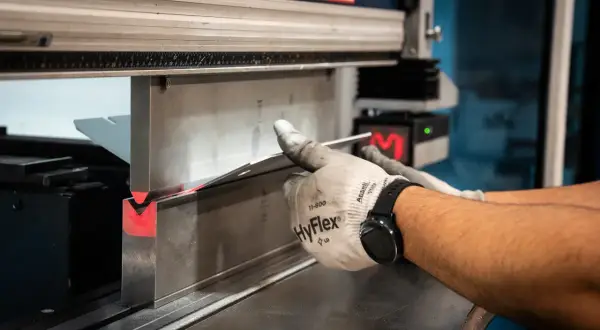 Operator w rękawicach formuje metal na prasie krawędziowej. Różne rodzaje prasy pozwalają na precyzyjne gięcie.